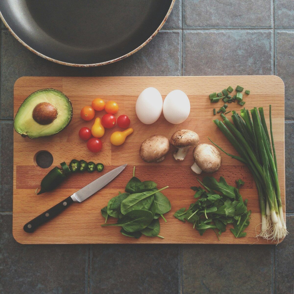 Avokado, tomater, ägg, svamp och salladslök på ett bord